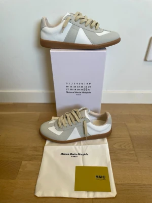 Maison Margiela gats beige/vit - Maison Margiela Replica sneakers i beige och vitt med klassisk gummisula. Ovandelen är i en mix av mocka och slätt läder, med beige snörning och diskreta detaljer. Snygg och tidlös modell som passar till det mesta.
