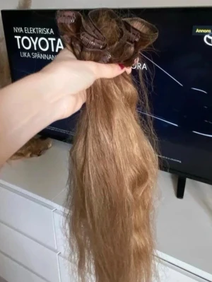 Ljusbruna clip-on löshår - Säljer ett set med ljusbruna clip-on löshår i vågig stil. Löshåret har flera clips för enkel fastsättning och är gjort av naturligt hår som kan stylas efter önskemål. Perfekt för dig som vill ha längre eller fylligare hår på nolltid.
