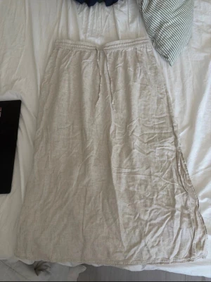 Beige långkjol från Pieces - Säljer en beige långkjol från Pieces i mjukt linnematerial. Kjolen har resår i midjan med knytband och en slits på sidan för extra rörelsefrihet. Perfekt för varmare dagar och enkel att styla med olika toppar.