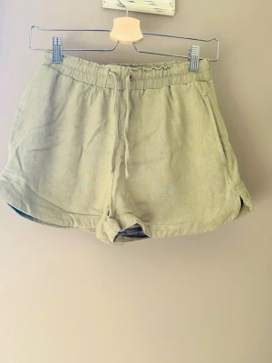 Gröna shorts med snörning - Snygga gröna shorts med elastisk midja och snörning framtill. De har en avslappnad passform och är tillverkade i ett mjukt linneliknande material, perfekta för varma dagar.