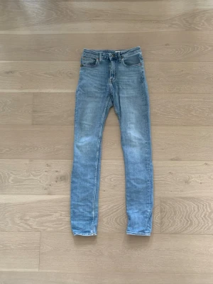 Tiger Of Sweden Jeans - Säljer ett par ljusblå skinny jeans med klassisk femficksdesign och normalhög midja. Jeansen har en snygg tvätt med lätt slitning på låren och raka benslut. Perfekta för en avslappnad och trendig look. Storlek 28/32