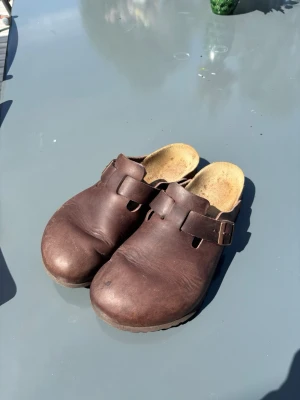 Birkenstock Boston - Säljer ett par Birkenstock Boston i brunt läder, storlek 43 (EU). Skorna är använda men i bra skick. Sulorna har fortfarande gott om mönster kvar och lädret är helt utan sprickor. Justerbart spänne för bra passform. Perfekta som vardagsskor, tofflor eller arbetsskor. Hör av dig vid intresse, pris är inte hugget i sten👌🏼