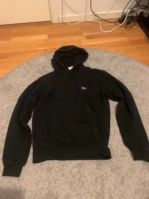 Svart hoodie från Lacoste - Säljer en svart hoodie från lacoste. Materialet känns mjukt och bekvämt.