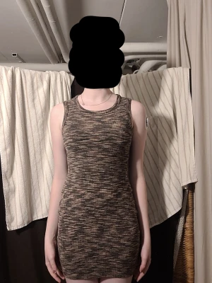 Ribbad brunmelerad ärmlös klänning - Säljer en tight, ribbad klänning i brunmelerad färg. Klänningen är kort, ärmlös och har rund halsringning. Materialet är stretchigt och följsamt, perfekt för dig som gillar en kroppsnära passform. Passar till många olika stilar och tillfällen. Xs-s