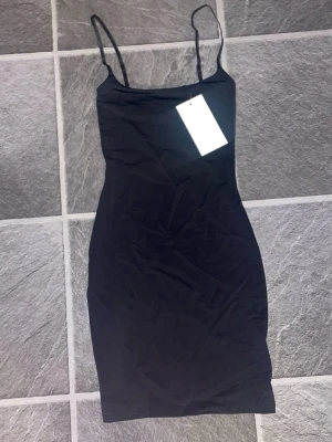 Svart tight klänning från Zara - Svart tight klänning från Zara med smala axelband och enkel, stilren design. Klänningen är kort och har en figurnära passform som framhäver siluetten. Perfekt för dig som gillar minimalistisk stil.