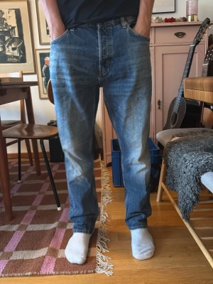 Blå raka jeans med hög midja - Säljer ett par klassiska blå jeans med rak passform och hög midja. Jeansen har fem fickor, gylf med dragkedja och knapp samt subtila slitningar för en avslappnad look. Perfekta till vardagsstilen och passar till det mesta.