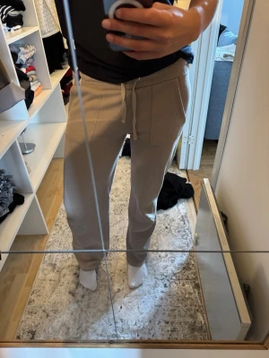 Beige mjukisbyxor  - Säljer ett par beige mjukisbyxor med dragsko i midjan och fickor både fram och bak. Byxorna har avslappnad passform och är gjorda i mjukt, stretchigt material som är perfekt för chill dagar. Snygga sömdetaljer framtill och resår i midjan för extra komfort.
