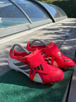 Röda och vita Adidas fotbollsskor - Säljer ett par snygga fotbollsskor från Adidas i rött och vitt med svarta detaljer. Skorna har klassisk snörning, låg profil och dobbar för gräsplan. Perfekta för dig som vill ha stilrena och funktionella skor på planen.