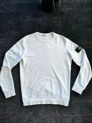 Stone Island sweatshirt - Säljer en clean vit sweatshirt från Stone Island med klassisk rund hals och lång ärm. Tröjan har den ikoniska Stone Island-loggan på vänster ärm och är gjord i mjukt bomullsmaterial. Perfekt för en stilren och avslappnad look. Skick 7/10 skavankerna syns på bilderna, storlek L. Pris går att diskutera✅