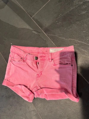 Rosa jeansshorts - Säljer ett par snygga rosa jeansshorts. De har klassisk femficksdesign, uppvikta benslut och knappgylf. Shortsen har broderade bakfickor och är perfekta för sommaren.