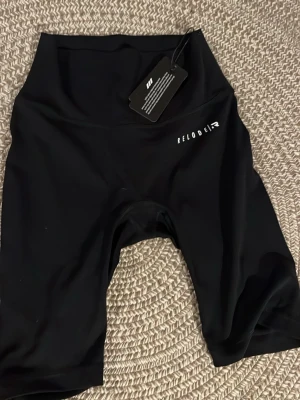 Svarta cykelshorts från Relode - Snygga svarta cykelshorts från Relode med hög midja och tight passform. Perfekta för träning eller en sportig look. Tillverkade i stretchigt syntetmaterial som ger bra rörelsefrihet. Helt oanvända passar xs/s