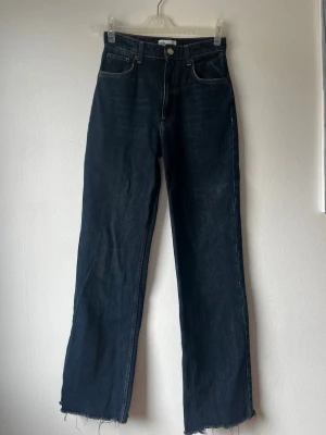 Långa Mörkblå raka jeans med rå kant 36/38 - Säljer ett par mörkblå jeans med rak passform och hög midja. Jeansen har råa, fransiga benslut och klassiska fem fickor