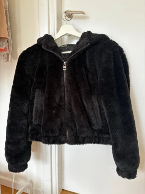 Svart pälsjacka med huva - Mjuk och fluffig svart pälsjacka från Pull&Bear med dragkedja framtill och huva. Jackan har långa ärmar och två sidofickor.