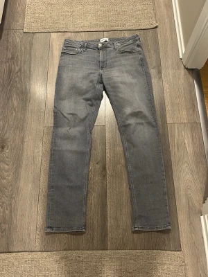 Gråa Regular Clark jeans - Snygga grå jeans i modellen Regular Clark med klassisk femficksdesign och raka ben. Jeansen har en ljusgrå tvätt och är tillverkade i mjukt denimtyg. Perfekta för en avslappnad och stilren look.