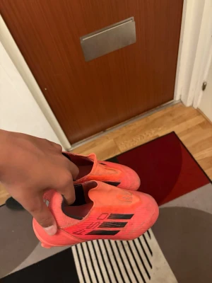 Adidas  fotbollsskor med dobbar f50 - Säljer ett par snygga fotbollsskor från Adidas i en stark rosa färg med svarta detaljer och klassiska tre ränder på sidan. Skorna har fasta dobbar för spel på gräs och är tillverkade i syntetmaterial för lätt vikt och bra passform. Perfekta för dig som vill sticka ut på planen!