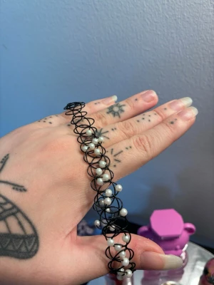 Svart chokerhalsband med pärlor - Unikt svart chokerhalsband i spiralformad plasttråd dekorerat med små vita pärlor. Halsbandet har en modern och edgy känsla, perfekt för att lyfta din stil med en cool detalj. Passar dig som gillar att sticka ut och vill ha något annorlunda.