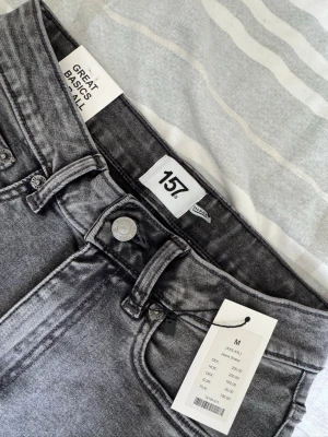 Grå slim fit jeans från 157 - Snygga grå slim fit jeans från 157 med klassisk femficksmodell och bälteshällor. Jeansen har en modern tvättad look och är tillverkade i stretchigt material för extra komfort. Perfekta för dig som gillar en stilren och enkel vibe.