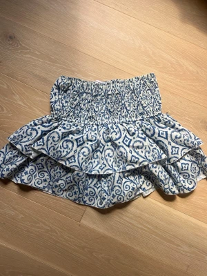 Meet Me There mönstrad kjol  - Supersöt kort kjol i vitt och blått med ett unikt mönster och bred smock i midjan. Säljer den eftersom den inte kommer till andvändning. Pris kan såklart diskuteras💞
