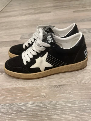 Golden Goose Ballstar sneakers svart/vit - Snygga Golden Goose Ballstar sneakers i svart mocka med vit stjärndetalj på sidan och vita skosnören. Skon har en retroinspirerad look med kontrasterande detaljer och texten 'SNEAKERS' på hälen. Insidan är vit och sulan har en vintagekänsla.