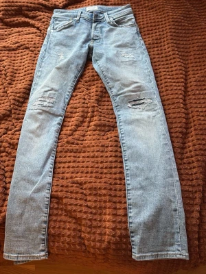 Ljusblå slitna skinny jeans - Säljer ett par ljusblå Slim fit jeans med slitningar på knäna och låren. Jeansen har klassisk femficksmodell, normal midja och dragkedjegylf. Perfekta för en avslappnad och trendig look.