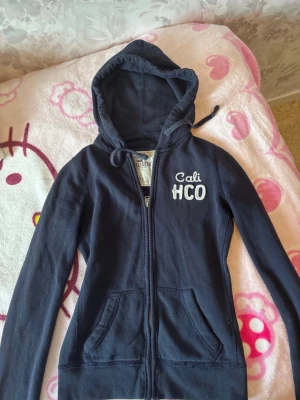Marinblå hoodie med dragkedja Hollister - En marinblå hoodie med dragkedja ifrån Hollister i storlek Xs.  Tydliga tecken på användning och defekter så som urtvättad, nopprig osv. Kvalitet syns på bilderna.  Skicka gärna prisförslag ❣️