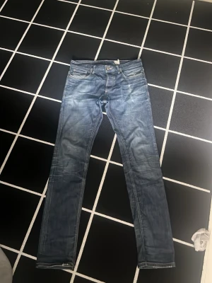 Blå slim fit jeans med slitningar - Säljer ett par blå slim fit jeans med snygga slitningar och tvättade detaljer. Klassisk femficksmodell med dragkedja och knapp i midjan. Jeansen har raka ben och är tillverkade i denim med lite stretch för skön passform.
