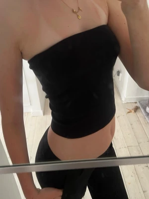 Svart bandeau tubtopp - En svart bandeau tubtopp med tight passform. Toppen är ärmlös och axelbandslös, perfekt för en stilren och enkel look. Materialet känns mjukt och stretchigt, vilket gör den bekväm att bära hela dagen.
