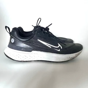 Svarta Nike React Miler Shield 2 - Snygga svarta Nike sneakers med vit, tjock sula och vit swoosh på sidan. Skorna har lågt skaft och är tillverkade i mesh och syntetmaterial för bra andningsförmåga. Perfekta för dig som gillar sportig och clean stil.