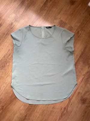 Ljusgrön blus från ONLY - Stilren ljusgrön blus från ONLY med rund halsringning och korta ärmar. Blusen har en diskret dragkedja i nacken och är tillverkad i ett lätt, mjukt tyg som faller snyggt. Perfekt till jeans eller kjol för en enkel men fräsch look.