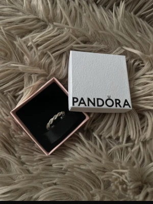 Silverfärgad ring från Pandora - Säljer en stilren silverfärgad ring från Pandora med ett flätat lövmönster. Ringen har en elegant design och kommer i original ask. Perfekt för dig som gillar klassiska smycken med en twist.