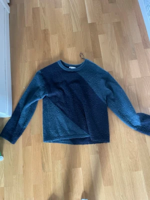 Mörkblå och blå stickad tröja - Säljer en stickad tröja i två nyanser av blått med diagonal färgblockdesign. Tröjan har rund halsringning och långa ärmar. Materialet är mjukt och fluffigt, perfekt för kyligare dagar.