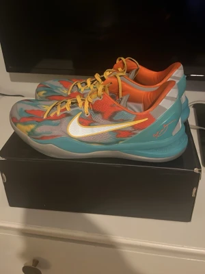 Kobe 8 Venice beach  - Färgglada Nike Kobe 6 Protro Grinch basketskor med mönstrad ovandel i rött, blått, gult och grått. Skorna har gula snören, vit Swoosh och orange insida. Låg modell med signaturdetaljer och slitstark sula, perfekta för basket eller streetwear. De är knappt använda dock limmat under sulan lite bara märks inte de är as snygga annars använda nån gång bara 