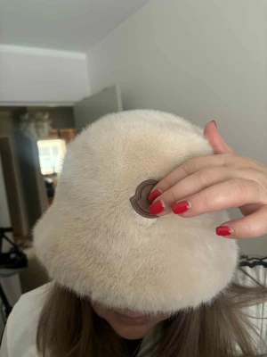 Beige fluffig bucket hat Moncler - Säljer en supermjuk och fluffig beige bucket hat.. Hatten har en rund form och är täckt av fuskpäls  Perfekt för dig som vill ha en trendig och mysig accessoar till höst och vinter.