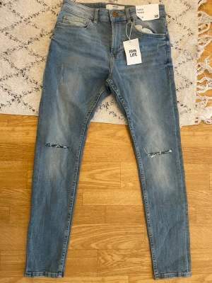 Blå skinny jeans med slitningar Zara - Säljer ett par ljusblå skinny jeans från Zara med slitningar vid knäna och klassisk femficksmodell. Jeansen har hög midja och är tillverkade i stretchigt denim för en bekväm passform. Perfekta för en avslappnad och trendig look.