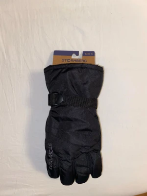 Svarta alpina handskar Stormberg S - Säljer ett par svarta alpina handskar från Stormberg, modell Vemdalen Alpine Gloves. Handskarna har justerbart band runt handleden och är tillverkade i ett slitstarkt syntetmaterial som håller värmen. Perfekta för kalla dagar i backen eller vinterpromenader.