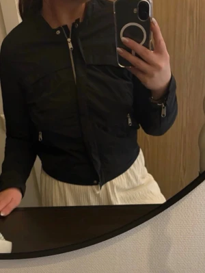 Peak performance jacka  - Snygg svart vindjacka med två framfickor med dragkedja och hög krage. Jackan har en rak passform och stängs med dragkedja framtill. Materialet är tunt och lätt, perfekt för blåsiga dagar. Passar till många olika stilar. Storlek M, rökfritt hem.