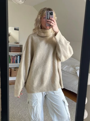 Oversize beige polotröja - En riktigt mysig och oversize stickad polotröja i beige. Tröjan har breda ärmar och ribbstickade detaljer vid hals, ärmslut och nederkant. Perfekt för lager-på-lager och chill stil. Materialet ser ut att vara mjukt och ulligt.