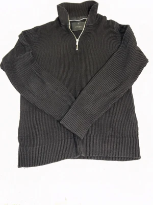 Svart Polotröja Jack&Jones med dragkedja - M - Säljer en svart ribbstickad tröja från Jack & Jones med hög krage och halv dragkedja framtill. Lite hål vid vänster arm/axel. Pris - 100kr. Storlek M.