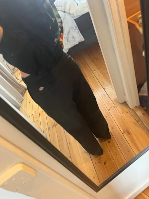 Svarta byxor från Dickies - Säljer ett par svarta byxor från Dickies med rak passform och hög midja. Går att vika ner för lägre midja och då syns den vita kanten med loggan. Klassisk Dickies-logga vid fickan och slitstarkt material som passar perfekt till en avslappnad streetwear-look.