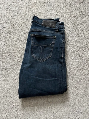 Mörkblå Jeans från Tiger Of Sweden - Snygga mörkblå jeans med raka ben och kontrastsömmar. Klassisk femficksmodell och läderpatch bak i midjan. Jeansen har en tidlös look och passar perfekt till en avslappnad stil. Materialet är denim i bomull.