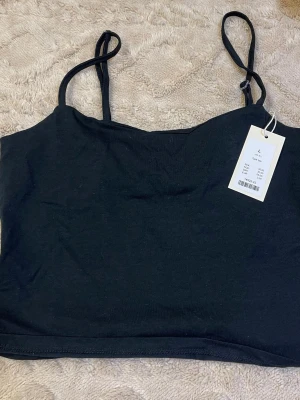 Svart ärmlös linnetopp - En enkel och stilren svart linnetopp med tunna axelband. Toppen har en rak passform och är tillverkad i mjukt bomullsmaterial. Perfekt att matcha med jeans eller kjol för en clean look.