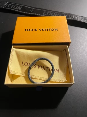Louis Vuitton armband i grå canvas - Snyggt armband från Louis Vuitton i grå canvas med metallspänne. Helt ny. Pris kan diskuteras vid snabb affär!