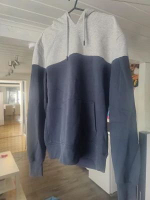 Tvåfärgad hoodie med ficka - Snygg hoodie i två färger, ljusgrå upptill och mörkblå nedtill. Har en stor magficka och justerbar huva med snören. Perfekt för en avslappnad och chill stil. Tillverkad i mjukt sweatshirtmaterial för extra komfort.