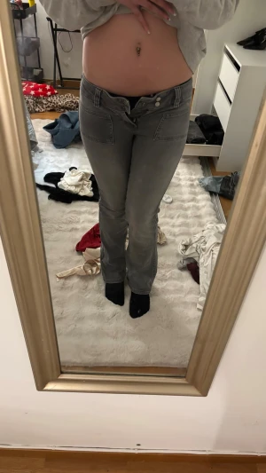 Grå bootcut jeans med låg midja - Säljer ett par gråa bootcut jeans med låg midja och klassiska fem fickor. Jeansen har en snygg tvättad look och stängs med dragkedja och knapp. Perfekta för dig som gillar retrovibbar och vill ha ett par bekväma jeans med lite utsvängda ben. Jag säljer dessa pågrund av att dom är försmå i midjan så kan inte spänna dom men har användt dom 1 gång så dom är i nytt skick.
