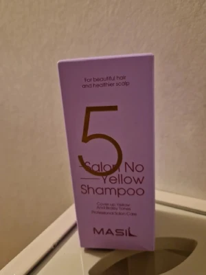 Masil 5 Salon No Yellow Shampoo - Lila förpackning med Masil 5 Salon No Yellow Shampoo, ett professionellt silverschampo som neutraliserar gula och brassy toner i håret. Perfekt för dig som vill ha kallare nyanser och ett fräscht resultat. Kommer i en stilren kartong med guldtext.
