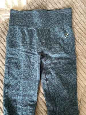 Tights Gymshark - Säljer ett par tights från Gymshark med diskret mönster, scrunch och hög midja. Tightsen har ett stretchigt material som sitter skönt och följer kroppens rörelser, perfekt för träning eller gym. Gymshark-logga i vitt på höften.