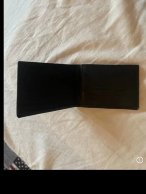 Svart klassisk läderplånbok - Snygg svart plånbok i äkta läder med flera kortfack och ett genomskinligt fack för ID eller foto. Plånboken har en stilren och tidlös design som passar perfekt i fickan. Enkel att öppna och stänga, och rymmer både kort och sedlar.