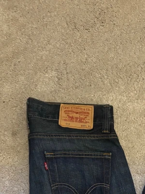 Levi's 512 Bootcut - Säljer ett par klassiska Levi's 512 Bootcut jeans i mörkblå denim med raka ben och snygga slitningar. Sköna fades med potential att bli ännu finare. Pris kan diskuteras vid snabbaffär!