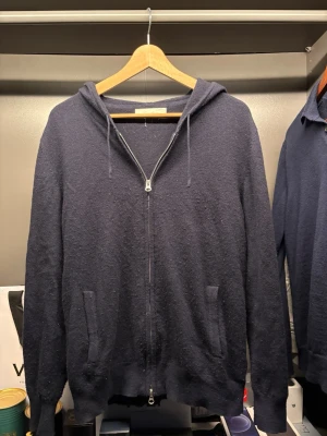 Mörkblå cashmere hoodie från Sayless - Mysig mörkblå hoodie i lyxig cashmere från Sayless. Tröjan har dragkedja framtill, två fickor och justerbar huva med snören. Perfekt för dig som vill ha något både stilrent och bekvämt. Passar till allt och känns riktigt skön mot huden.