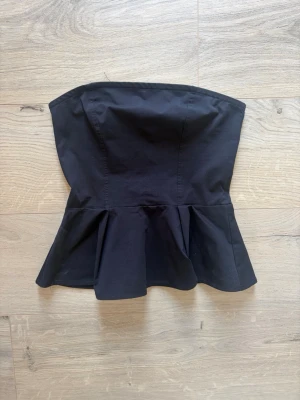 Svart bandeoutopp H&M Xs - Snygg svart bandeoutopp från H&M. Toppen har en figurnära passform upptill och en utsvängd volang nedtill. Perfekt att styla med jeans eller kjol för en trendig look.